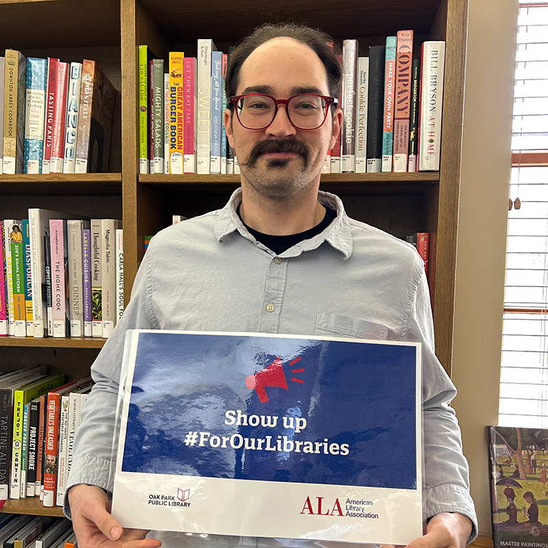 Library staff member holding a sign that reads, Show up #ForOurLibraries
