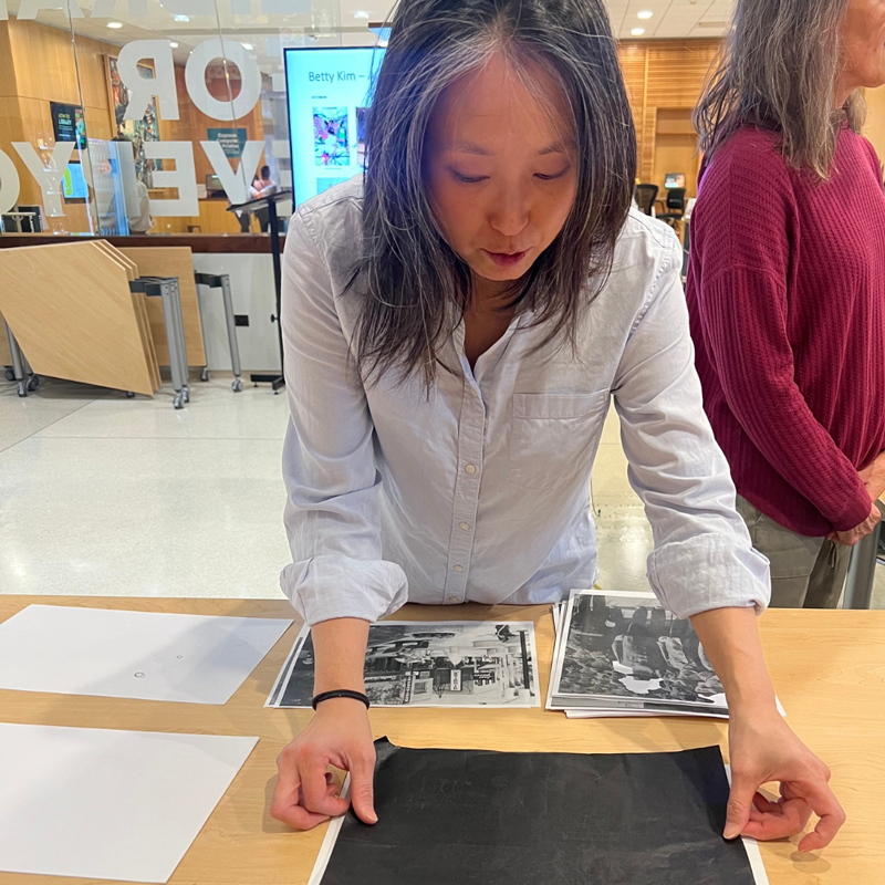 Artist Betty Kim tapes carbon copy paper down on a table at the library
