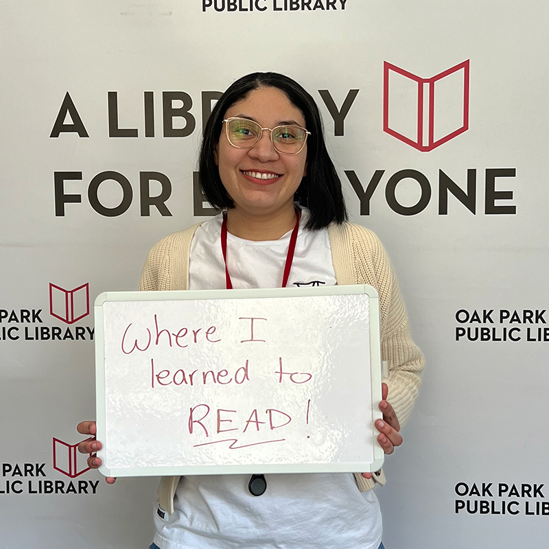 Library staff member holding a sign that reads, Where I learned to read