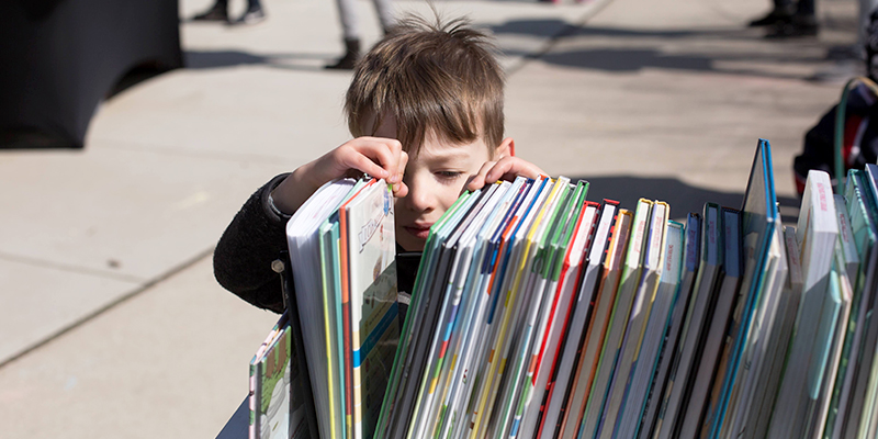 Child looks through a row of picture books outdoors