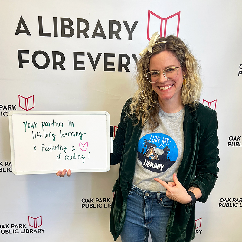 Library staff member holding a sign that reads, Your partner in lifelong learning and fostering a love of reading.