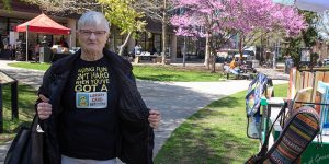 Person shows off their T-shirt that says "Having fun isn't hard when you've got a library card" while standing outside the Main Library.