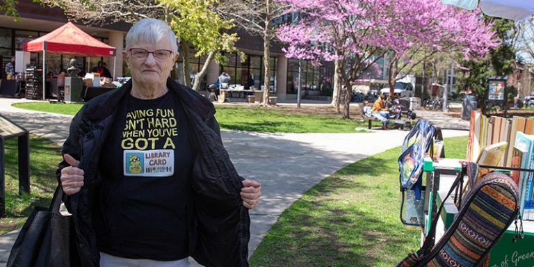 Person shows off their T-shirt that says "Having fun isn't hard when you've got a library card" while standing outside the Main Library.