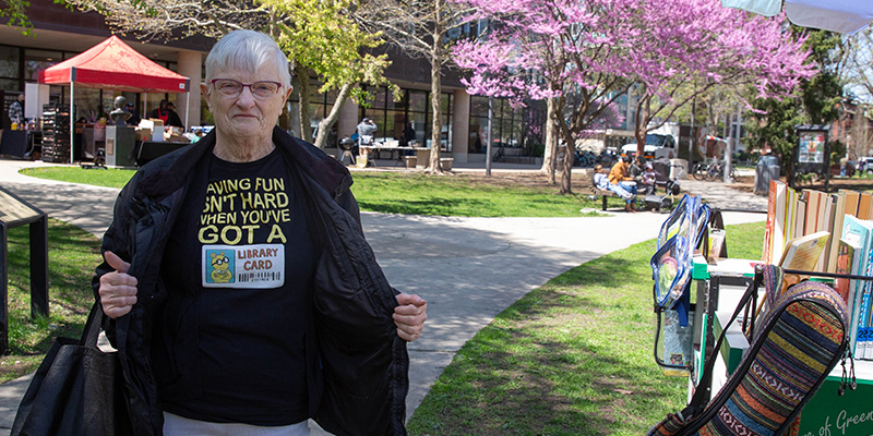 Person shows off their T-shirt that says "Having fun isn't hard when you've got a library card" while standing outside the Main Library.