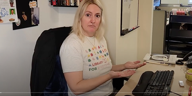 Librarian sits at a desk and does not have a book in their hands.