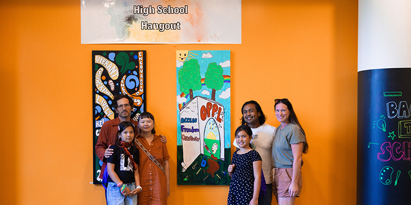 Kids and families involved in Mural Makers group pose next to the mural they created.