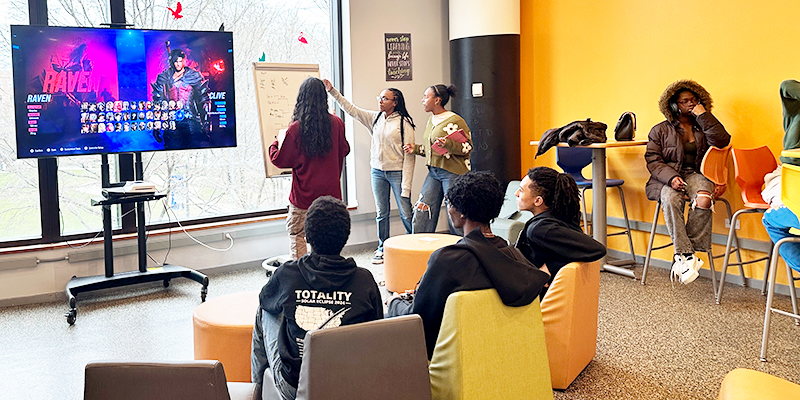 Teens play video games in the library on a big-screen TV.