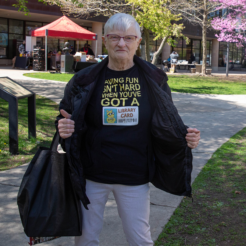 Person shows off their T-shirt that says Having fun isn't hard when you've got a library card while standing outside the Main Library.