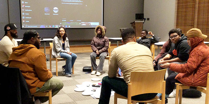 A group of students and adults sit on chairs in a circle, talking.