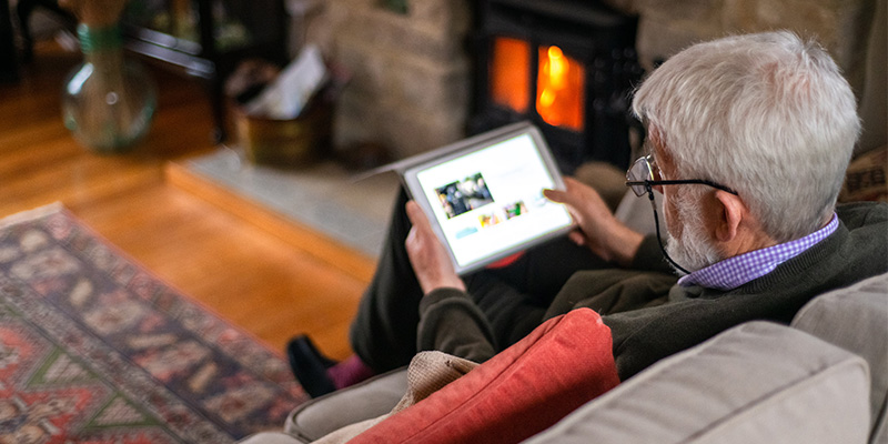 Person sits on a couch next to a fireplace and looks at a tablet computer.