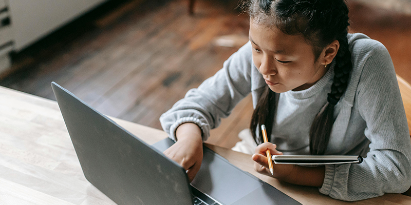 Student studying while holding a notebook and pencil and interacting with a laptop.