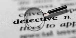 A magnifying glass over the word detective on a printed dictionary page.