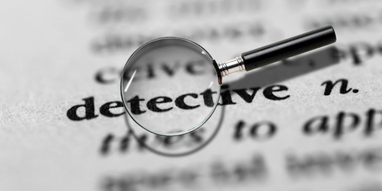 A magnifying glass over the word detective on a printed dictionary page.