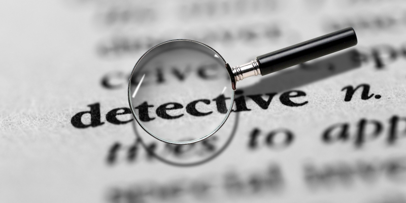 A magnifying glass over the word detective on a printed dictionary page.
