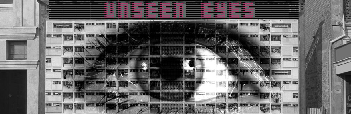Sidewalk scene of two buildings with a wall between them showing a gigantic eye, text reading Unseen Eyes, and two large cameras on top.