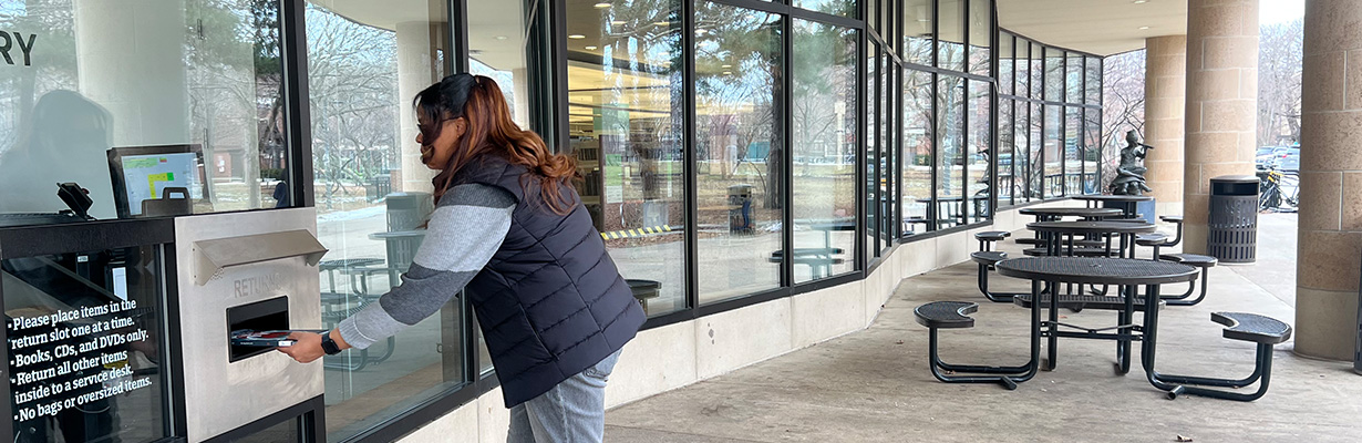 Person returns books to a window on the exterior of the Main Library building.