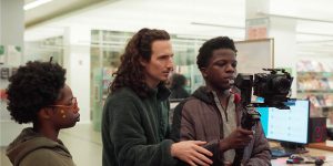 Two students and an adult with video equipment in the library.