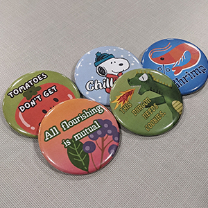 Five buttons on a table. The top one has cartoon pictures of plants and says All flourishing is mutual.