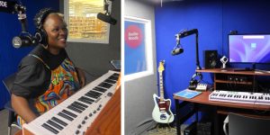 Person wears headphones with microphones pointing at them in a recording booth. Also the booth has a guitar, keyboard, and computer monitor.